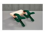 Two green spring clamps holding a piece of light wood on a grey surface.