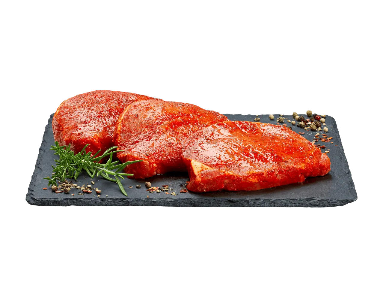 Trois steaks de porc marinés avec du romarin et des grains de poivre sur une planche d'ardoise.