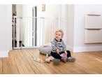 A baby sitting on a wooden floor, playing with toys, next to a white safety gate.