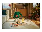 Child in Christmas sweater playing with a wooden train set and construction vehicles.