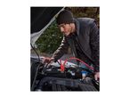 A man using red and black jumper cables to jump-start a car battery under the open hood.