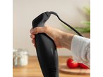 Hand houdt een zwarte staafmixer met snoer vast, met tomaten op de achtergrond.