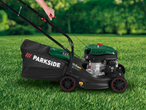 Person mowing a green lawn with a black and green petrol lawnmower.