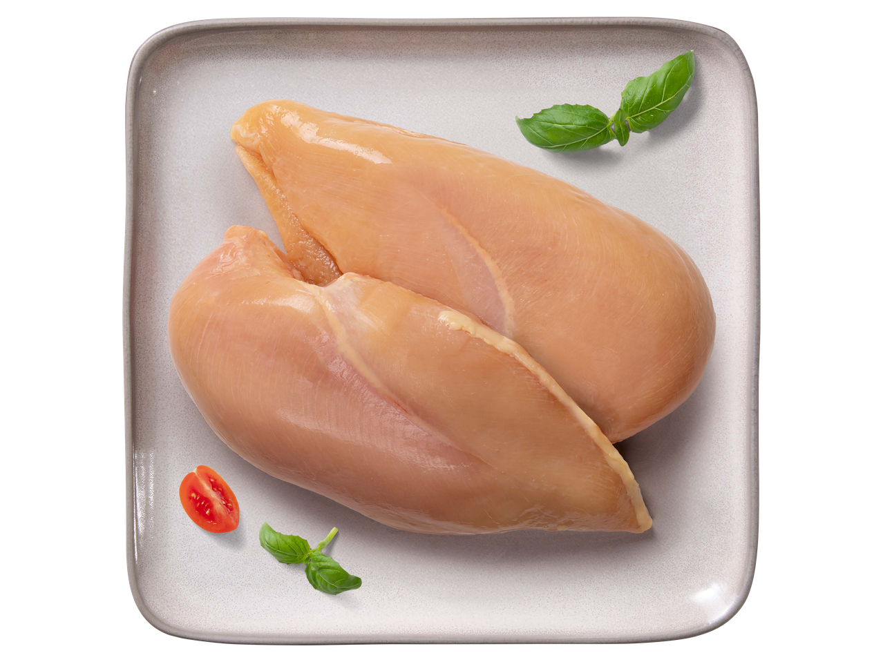 Két darab friss, nyers csirkemellfilé tálalótányéron, bazsalikommal és paradicsommal díszítve.