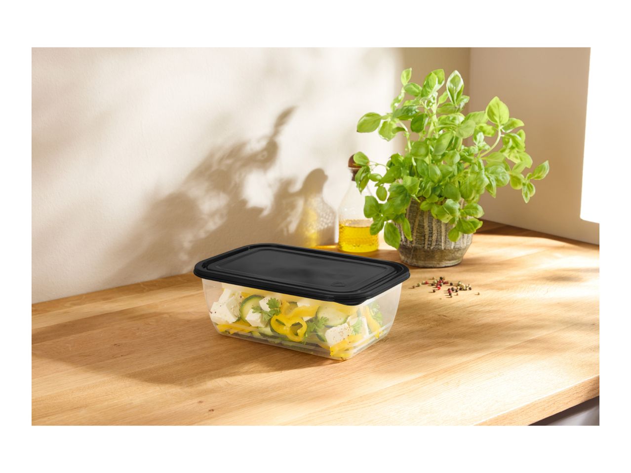 Clear food container with black lid, filled with salad, on a wooden counter.