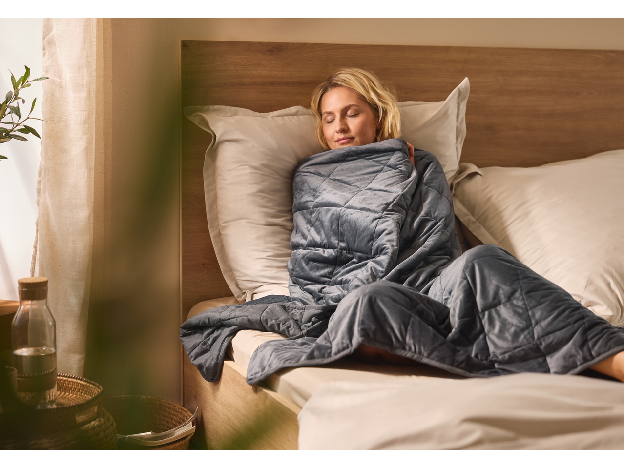 Relaxed woman in bed, wrapped in a gray weighted blanket.