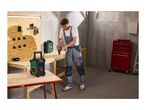 Man in overalls using a drill at a workbench with a portable radio and tool case.