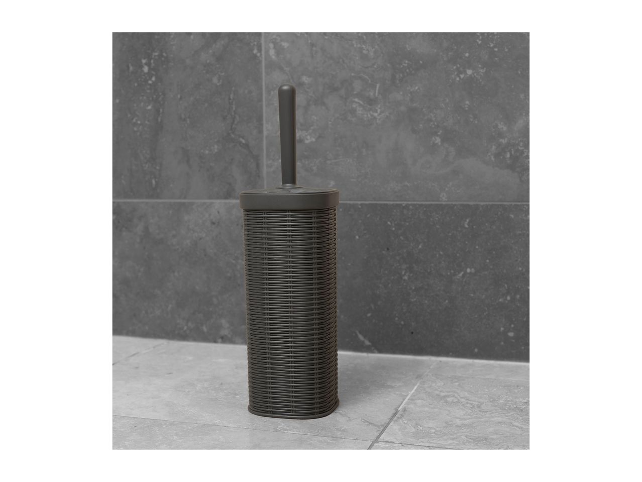 Dark grey toilet brush with a woven texture holder on a tiled bathroom floor.