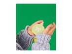 Hands in a knitted sweater holding a light green perfume bottle with a bow design.