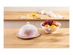 A white mesh food cover over a cake slice on a plate, next to a bowl of fresh fruit.