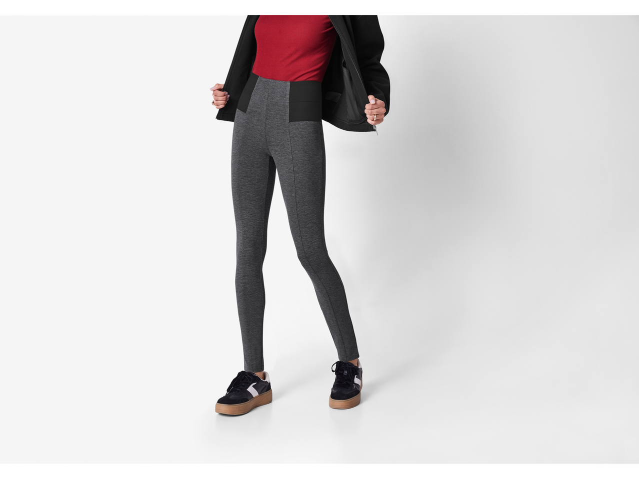 Femeie purtând jeggings modelatoare Esmara gri, un top roșu și o jachetă neagră, cu adidași negri.