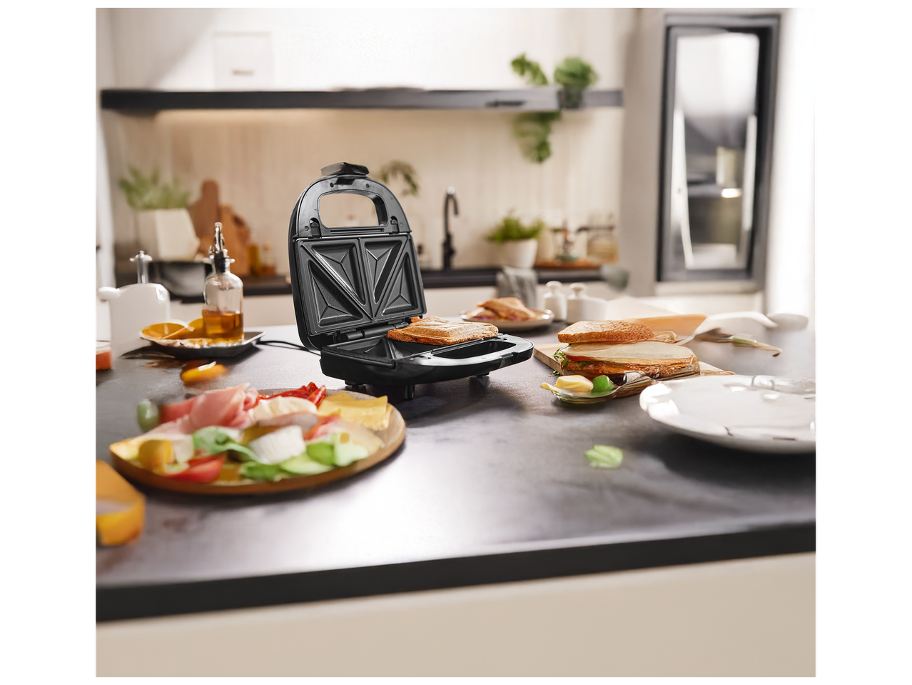 Gaufrier ouvert avec un sandwich grillé, entouré d'ingrédients frais sur un comptoir de cuisine.