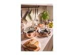 Copper-colored pots and pans on a kitchen counter with fresh bread and basil.