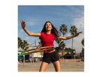 Smiling girl in red top and black shorts hula hooping outdoors with palm trees in background.