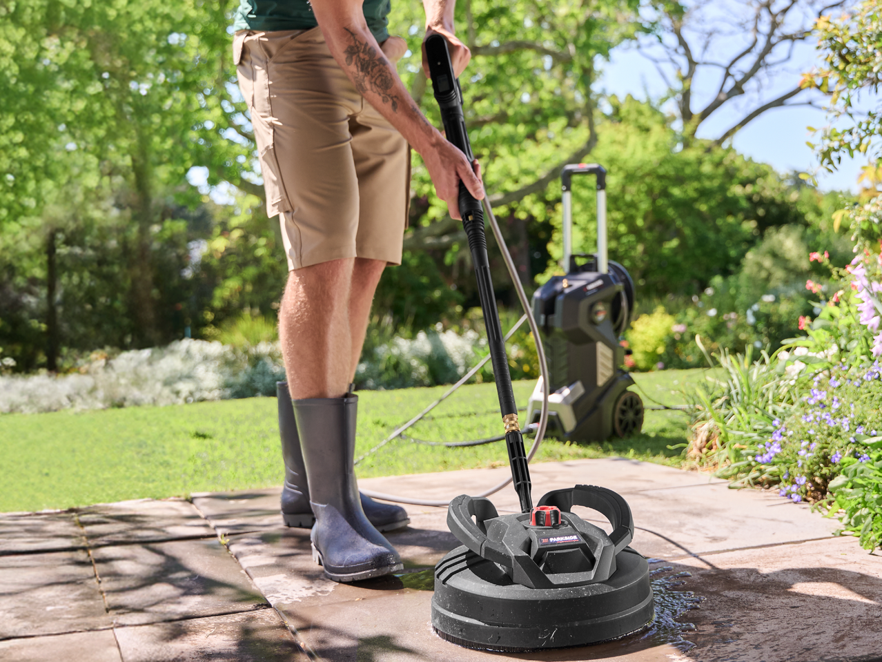 Мъж почиства вътрешен двор с уред за почистване под налягане и приставка за повърхности.