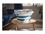 Foldable laundry basket with folded clothes on a wooden table in a living room.