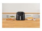 Black air fryer on a wooden counter with chicken nuggets, brussels sprouts, and fries.