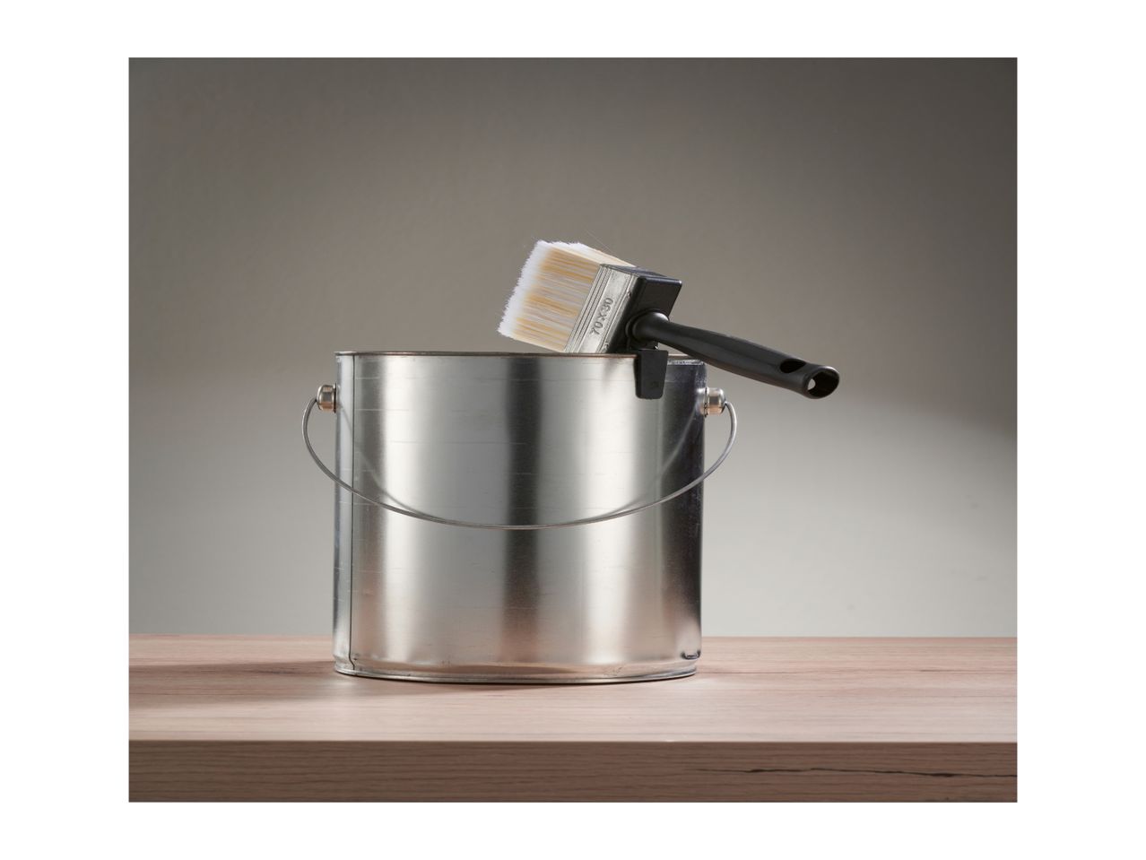 Paint can with a paintbrush resting on its rim, on a wooden surface.