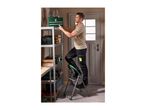 Man on a step stool placing a green toolbox on a metal shelving unit in a garage.