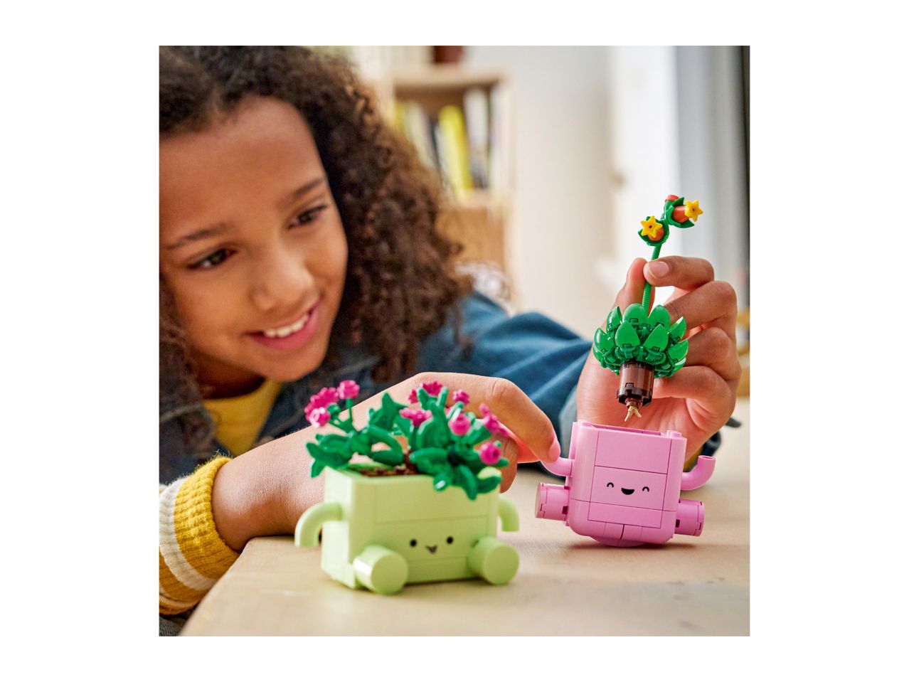 A smiling child plays with two colorful toy plant pots with faces, one green and one pink.