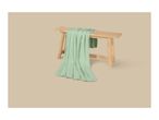 Light green blanket draped over a wooden bench on a beige background.