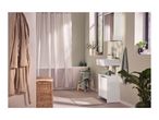 A modern bathroom with a white sink, cabinet, and bathtub, featuring green towels and plants.