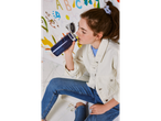 A girl sits on the floor, drinking from a Contigo water bottle against a colorful wall.
