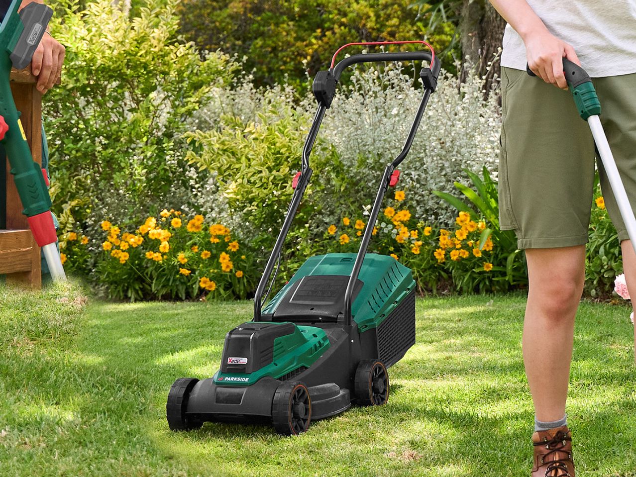 A person using a lawnmower and another holding a grass trimmer in a sunny garden.
