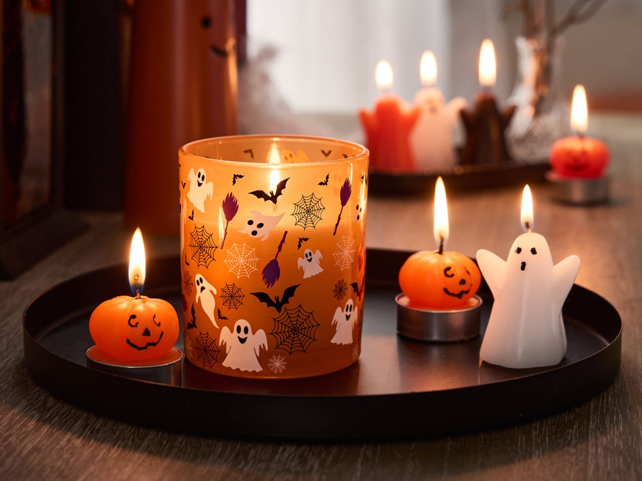Halloween-themed candles, including a ghost, pumpkins, and a jar with spooky decals, on a black tray.