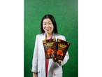 A woman holding two bags of Fleur de Lan Croissant Crisps against a green background.