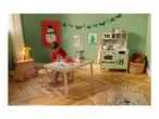 Child playing with a toy kitchen and food on a table in a Christmas-decorated room.