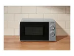 A microwave oven with two control dials on a wooden countertop against a tiled wall.