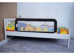 White toddler bed with a black and mesh bed rail, colorful bedding, and a teddy bear.