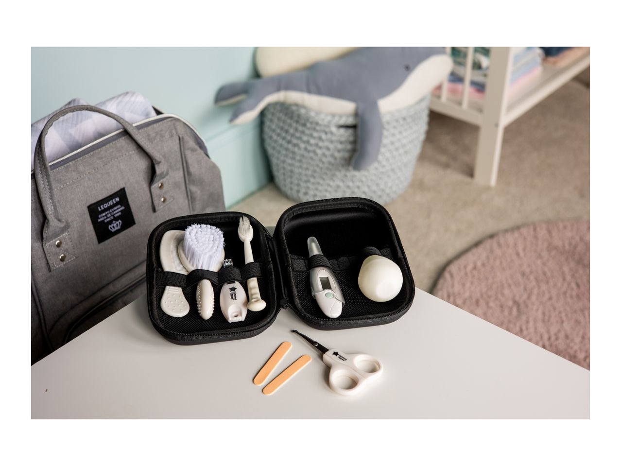 Baby care kit with brush, comb, nail clippers, thermometer, and scissors on a white table.