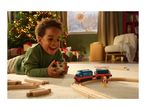 A happy child plays with a toy train set on a rug, with a Christmas tree in the background.