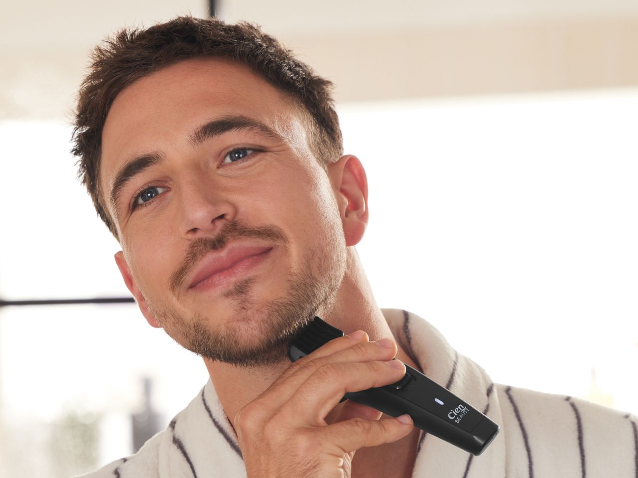 Man using a beard trimmer in a bathroom.