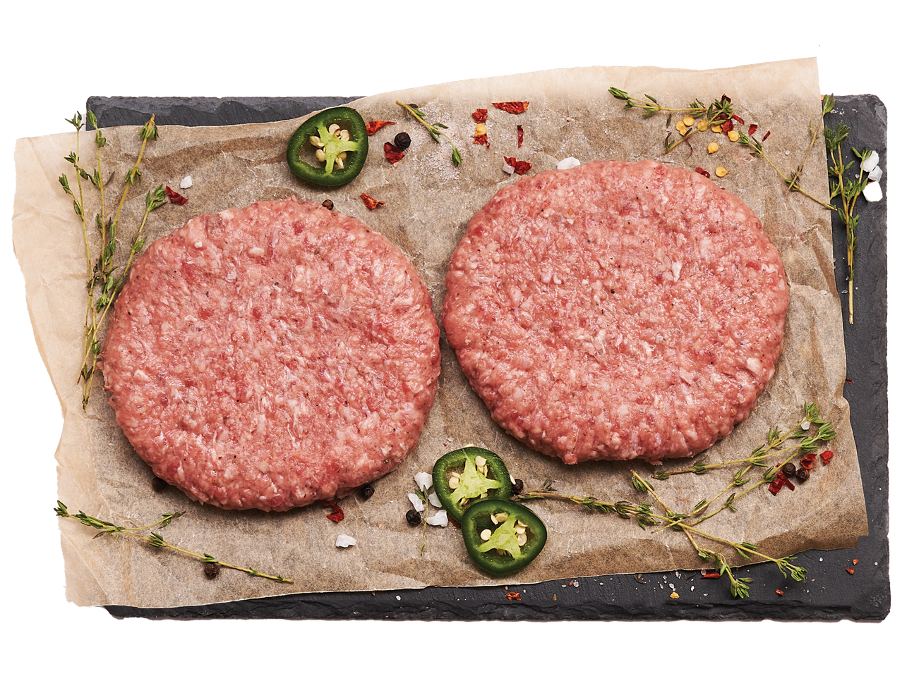 Две сурови телешки кюфтета с мащерка, люти чушки и подправки върху хартия за печене.