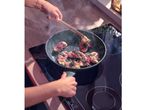 A person cooking bacon-wrapped chicken with sage in a frying pan on an induction hob.