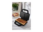 Waffle maker with two golden waffles, and a plate of waffles with berries and powdered sugar.