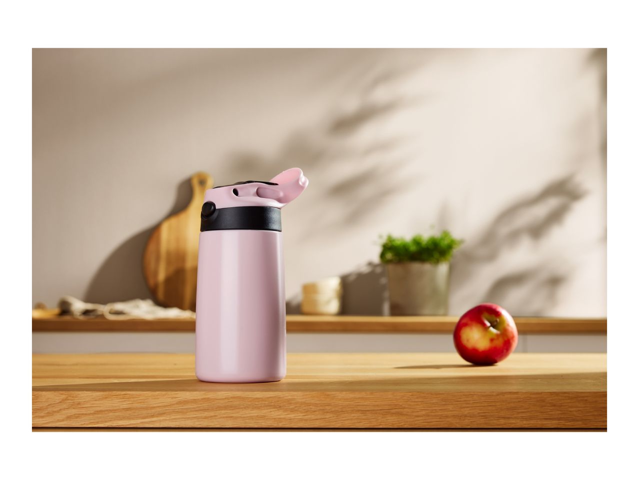 Pink water bottle with a red apple on a wooden kitchen counter