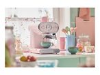 Pink SilverCrest espresso machine brewing coffee in a pastel-themed kitchen.