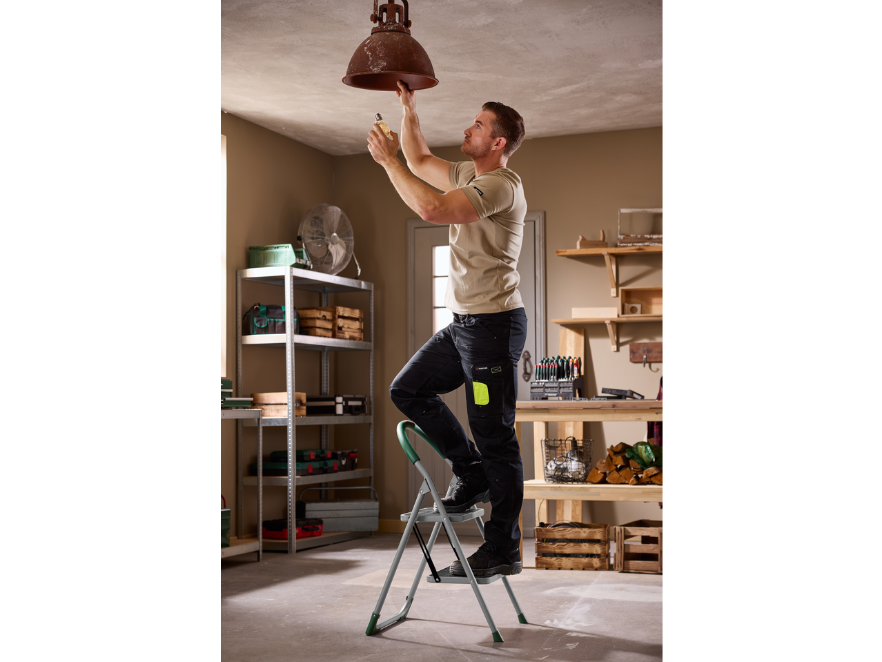 Muškarac na PARKSIDE® ljestvama mijenja žarulju u radionici.