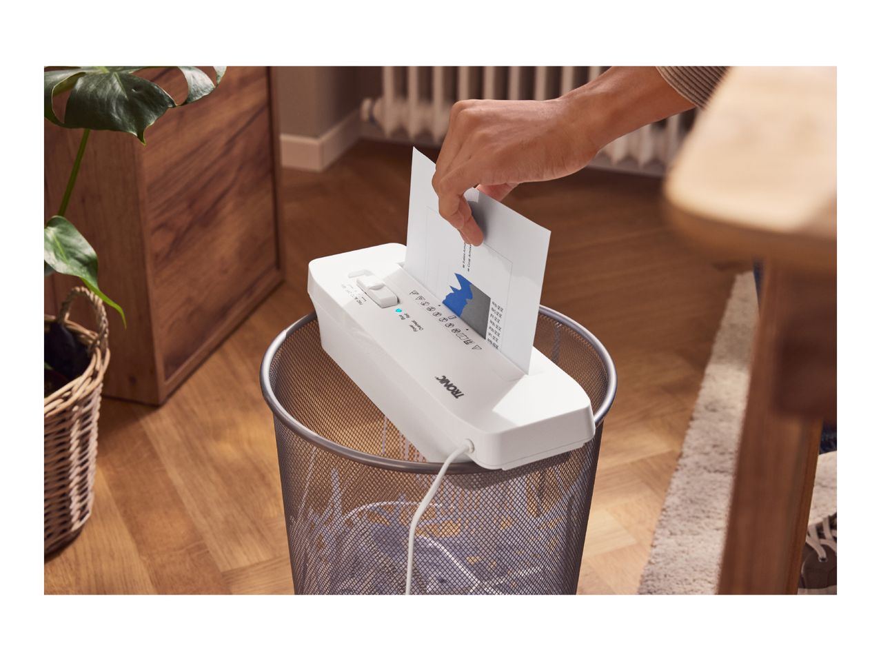 A person shredding a document with a TRONIC paper shredder placed on a waste bin.