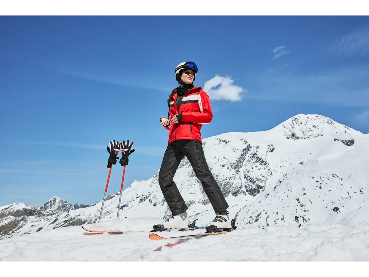 Woman in red Crivit ski jacket and black pants, skiing on a snowy mountain.