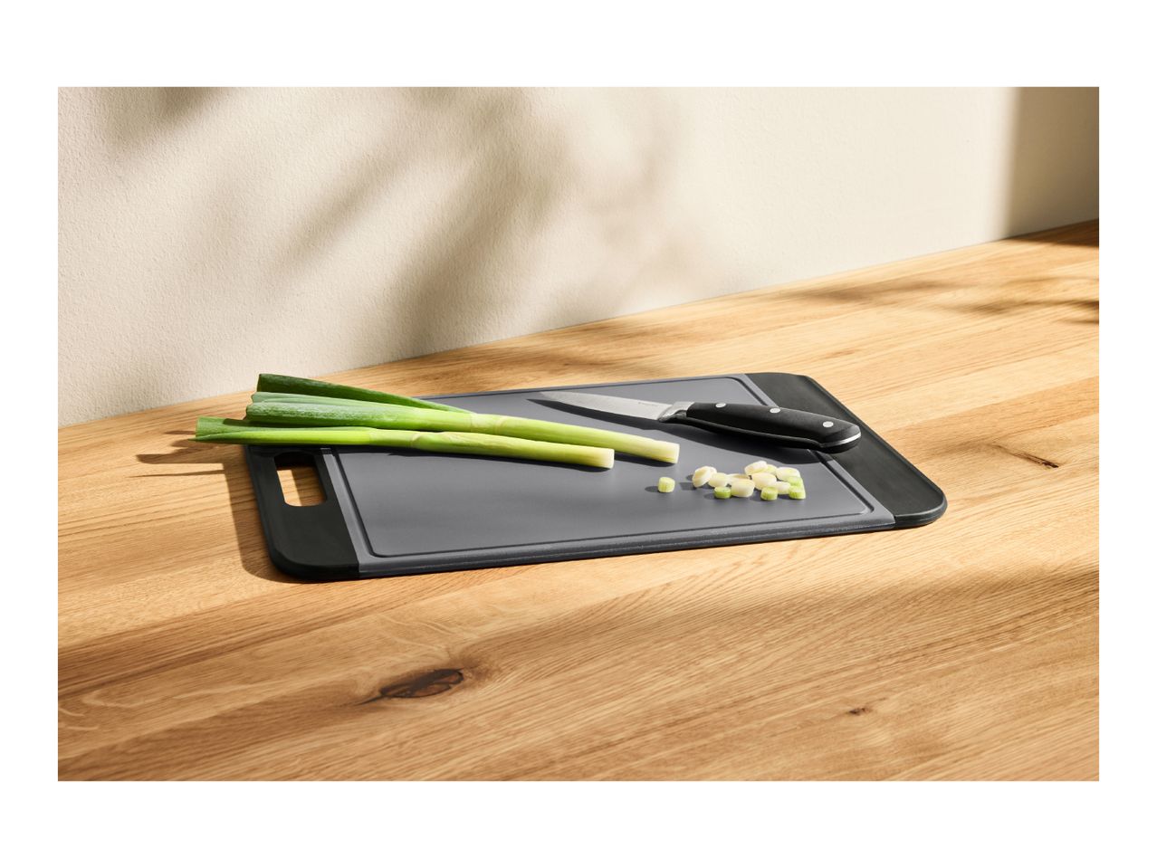 A grey cutting board with green onions and a knife on a wooden table.