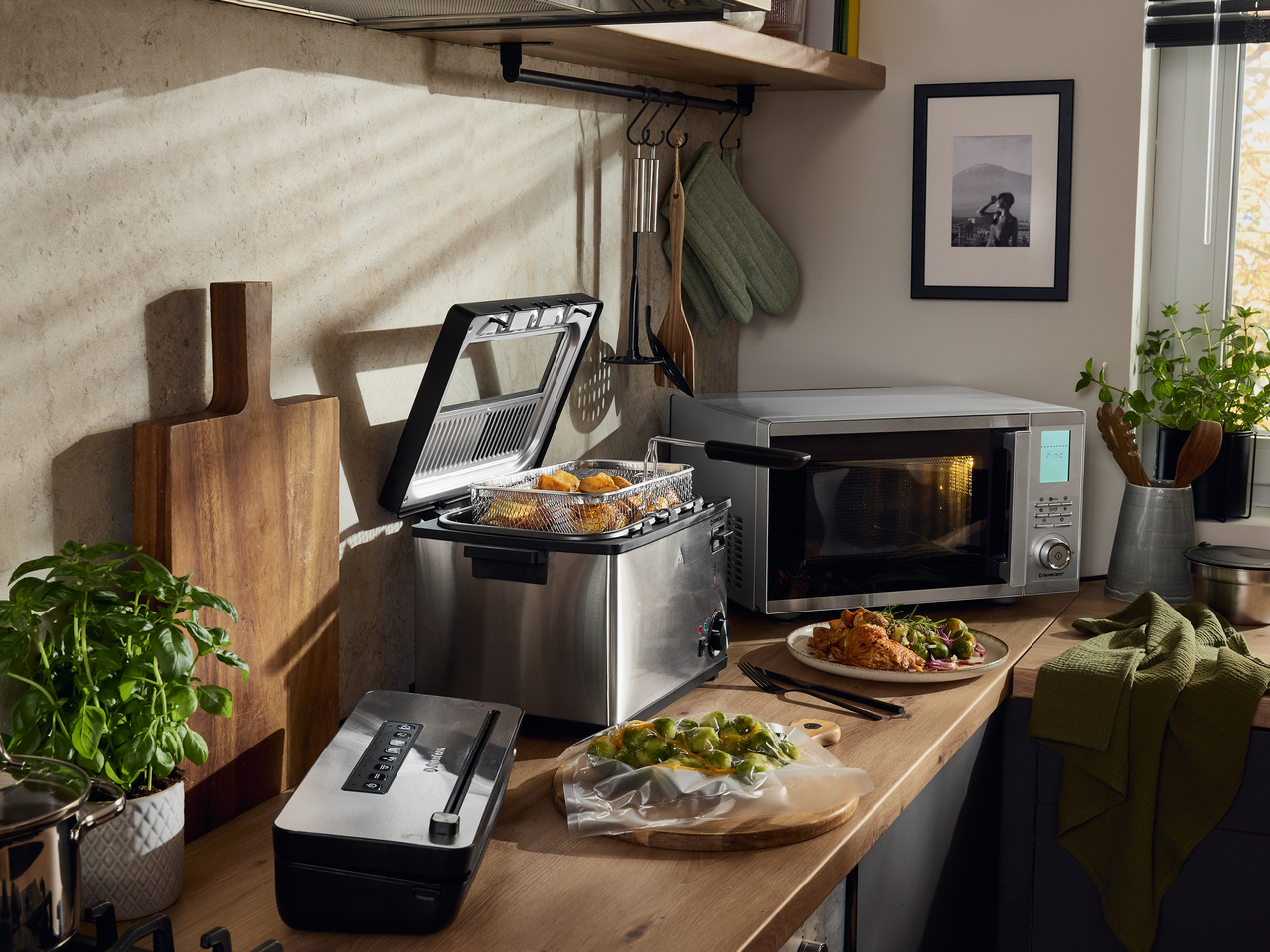 Πάγκος κουζίνας με φριτέζα, φούρνο μικροκυμάτων και συσκευή κενού, που ετοιμάζει ένα γεύμα.