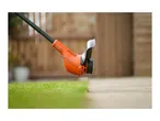 Orange grass trimmer cutting an edge between grass and pavement in a garden.