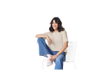 Mulher sorridente sentada em uma cadeira branca usando jeans e tênis.