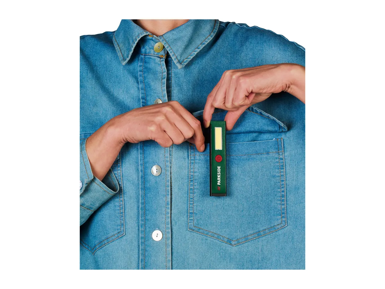 Person in denim shirt putting a green Parkside work light into a pocket