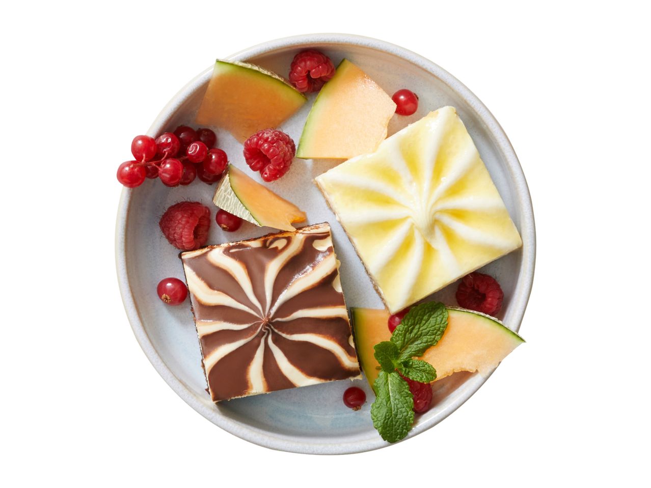 Two dessert slices with melon, raspberries, and redcurrants on a plate.